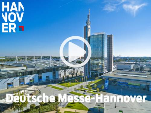 Luftaufnahme der Deutschen Messe Hannover mit Glasbürogebäude, Funkturm und Messehallen mit markanter Dachkonstruktion.